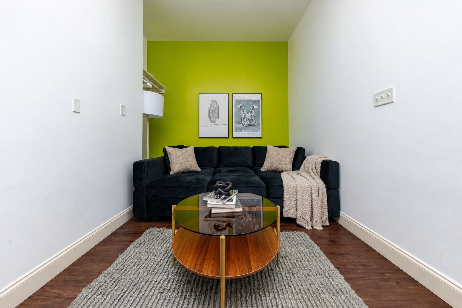 A living room with a dark sofa, a glass coffee table, and a green accent wall.