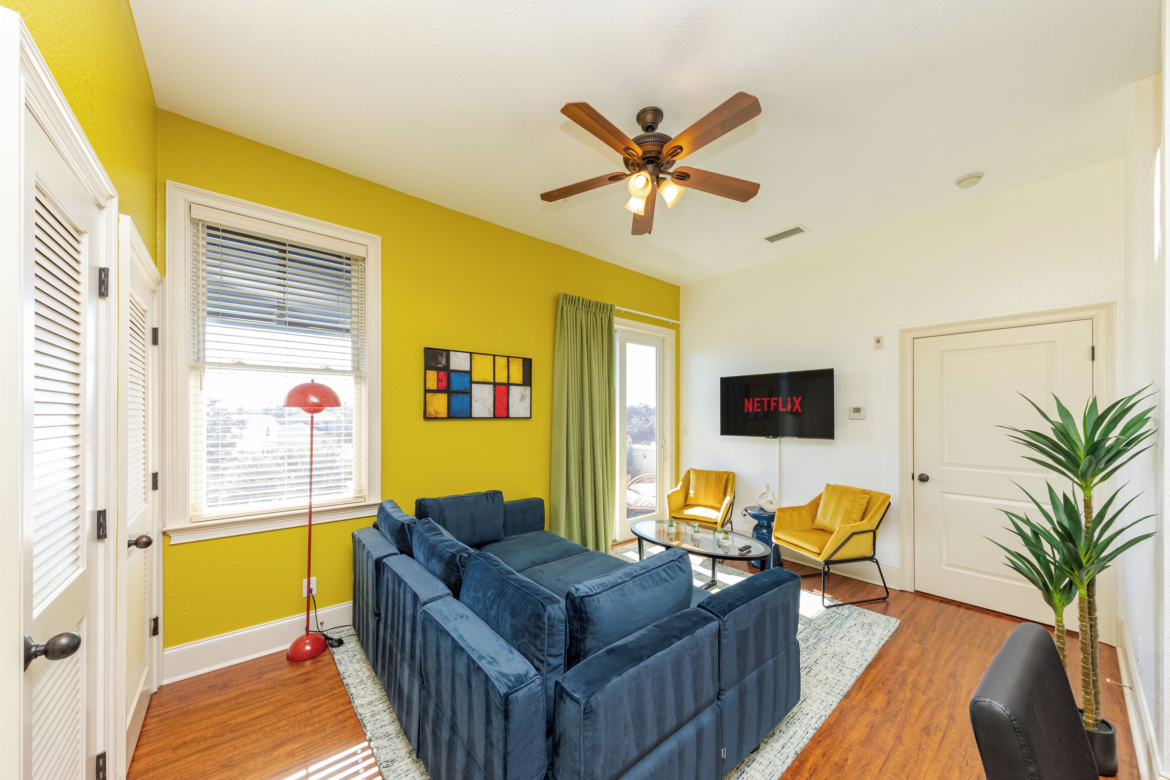A living room with a sectional sofa, a ceiling fan, a TV mounted on the wall, and a door.