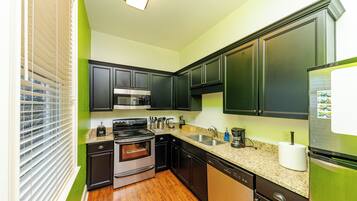 Et lille køkken med mørke skabe, et rustfrit stål køleskab, en mikrobølgeovn og en opvaskemaskine.