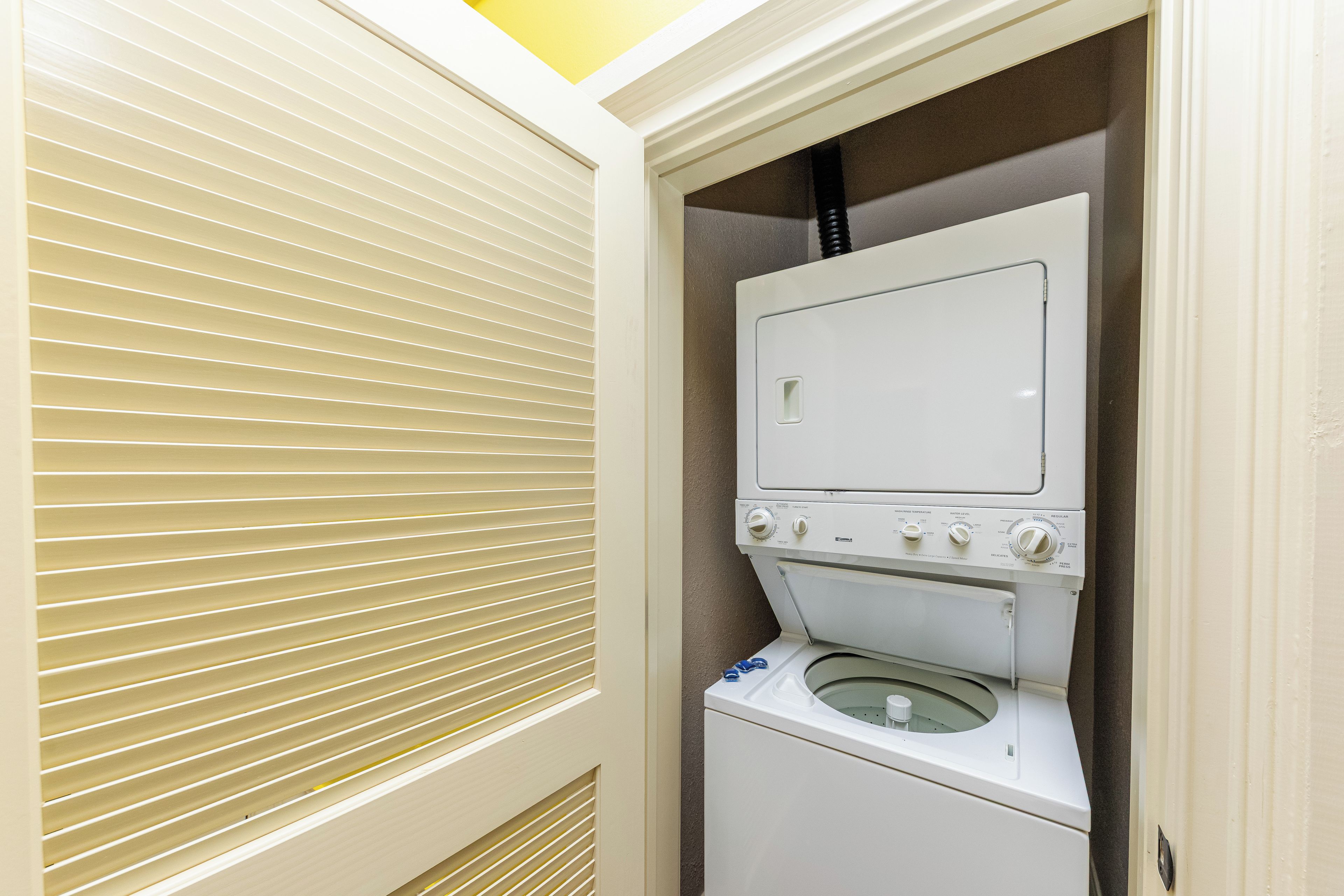 Een wasserette met een voorlader wasmachine en droger, een ventilatieopening en een deur met zonwering.