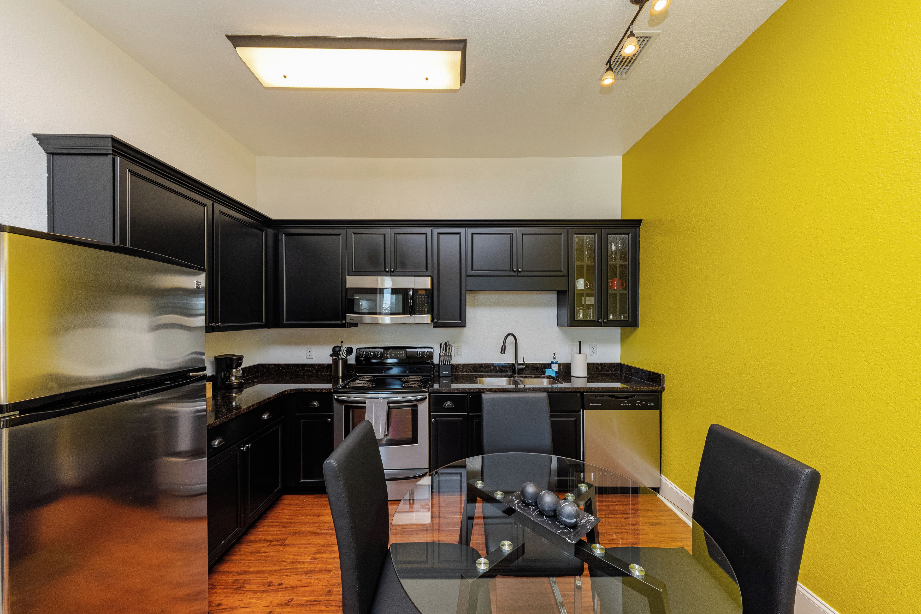 A modern kitchen with black cabinets, stainless steel appliances, and a glass dining table.