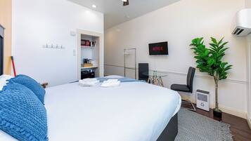 Una habitación de hotel moderna con cama, ventilador de techo, televisor, planta y una pequeña mesa.