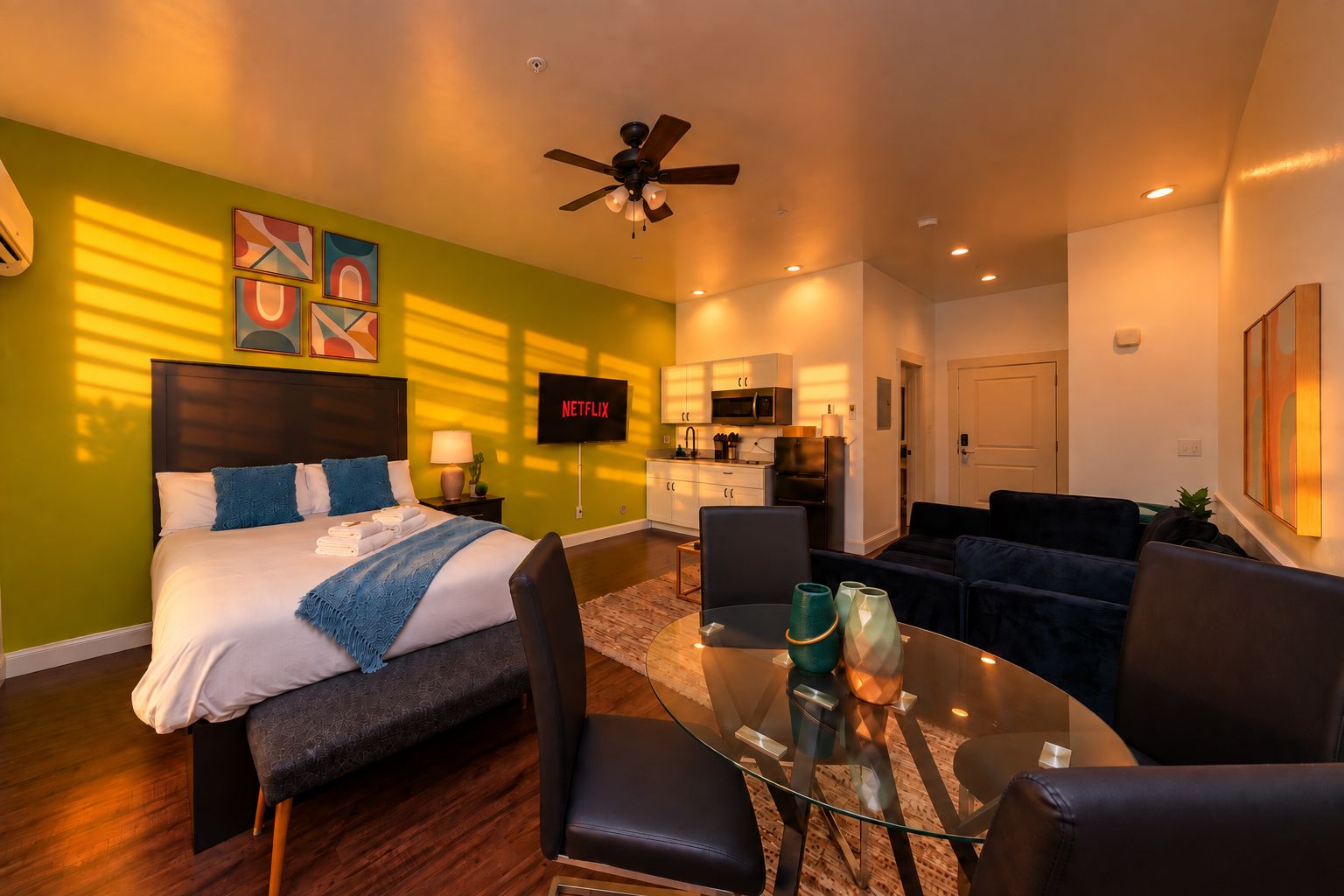 Une chambre d’hôtel moderne équipée d’un lit, d’un coin salon, d’une kitchenette et d’un téléviseur affichant l’application « NETFLIX ».