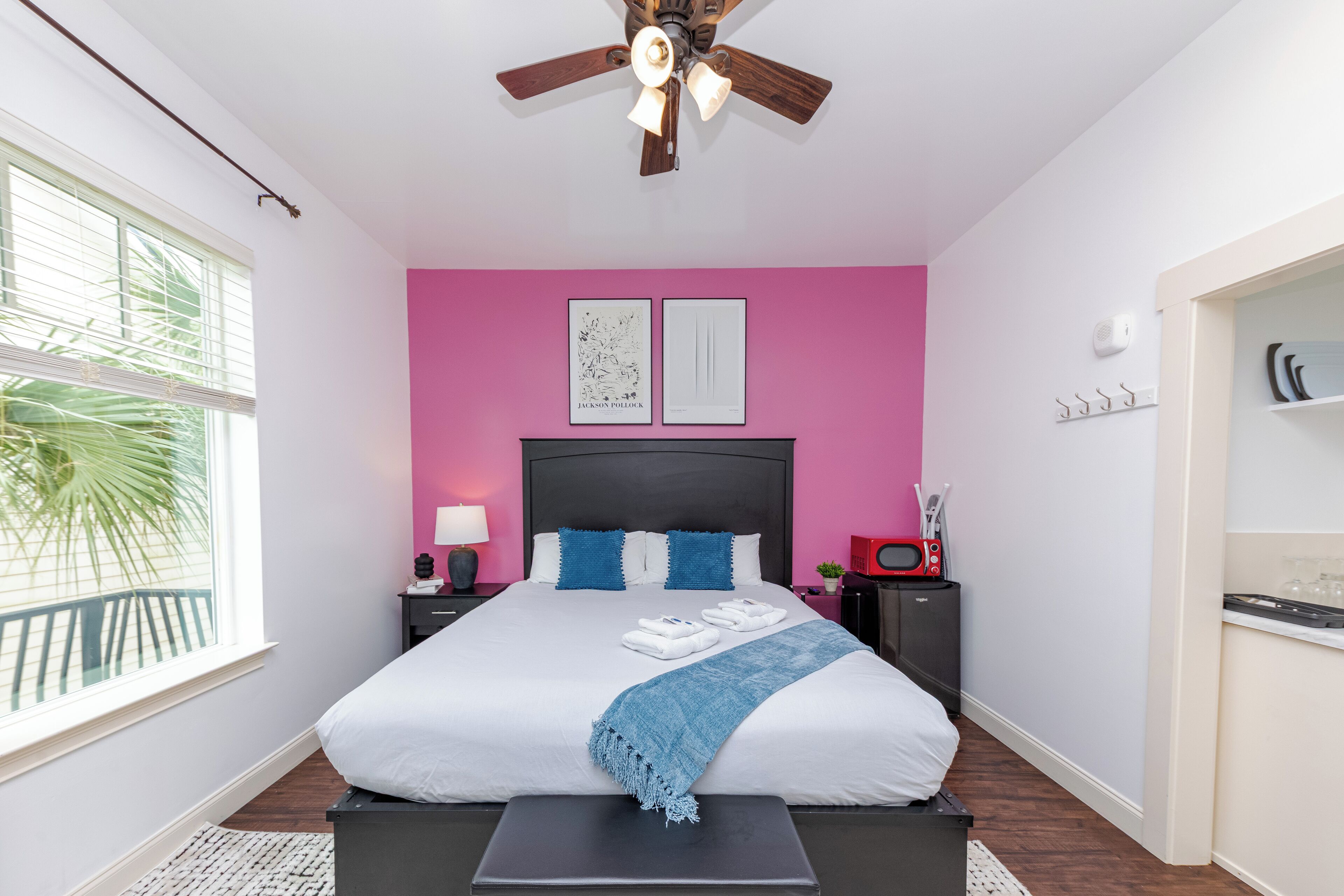 Un dormitorio con cama, ventilador de techo, mesita de noche, lámpara y ventana con persianas.