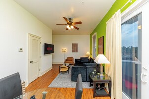 A living room with a ceiling fan, a black sofa, a glass coffee table, and a TV on the wall.