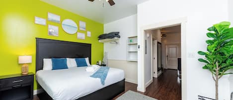 Ein modernes Schlafzimmer mit Bett, Nachttisch, Wanduhr und Deckenventilator.