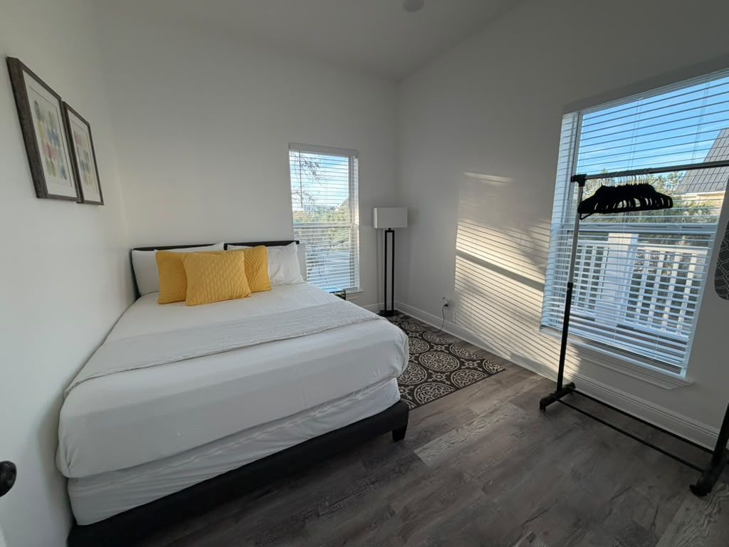 A bedroom with a bed, a floor lamp, a patterned rug, and a window with blinds.