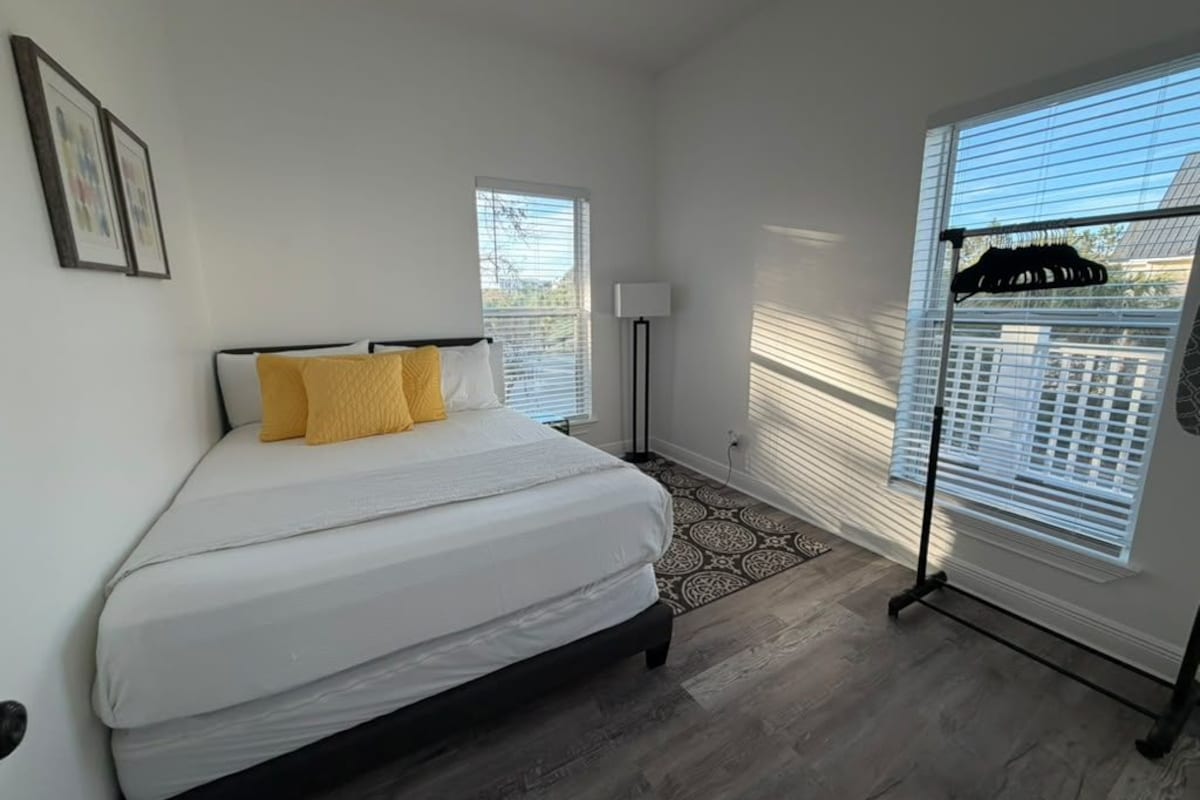 A bedroom with a bed, a floor lamp, a patterned rug, and a window with blinds.