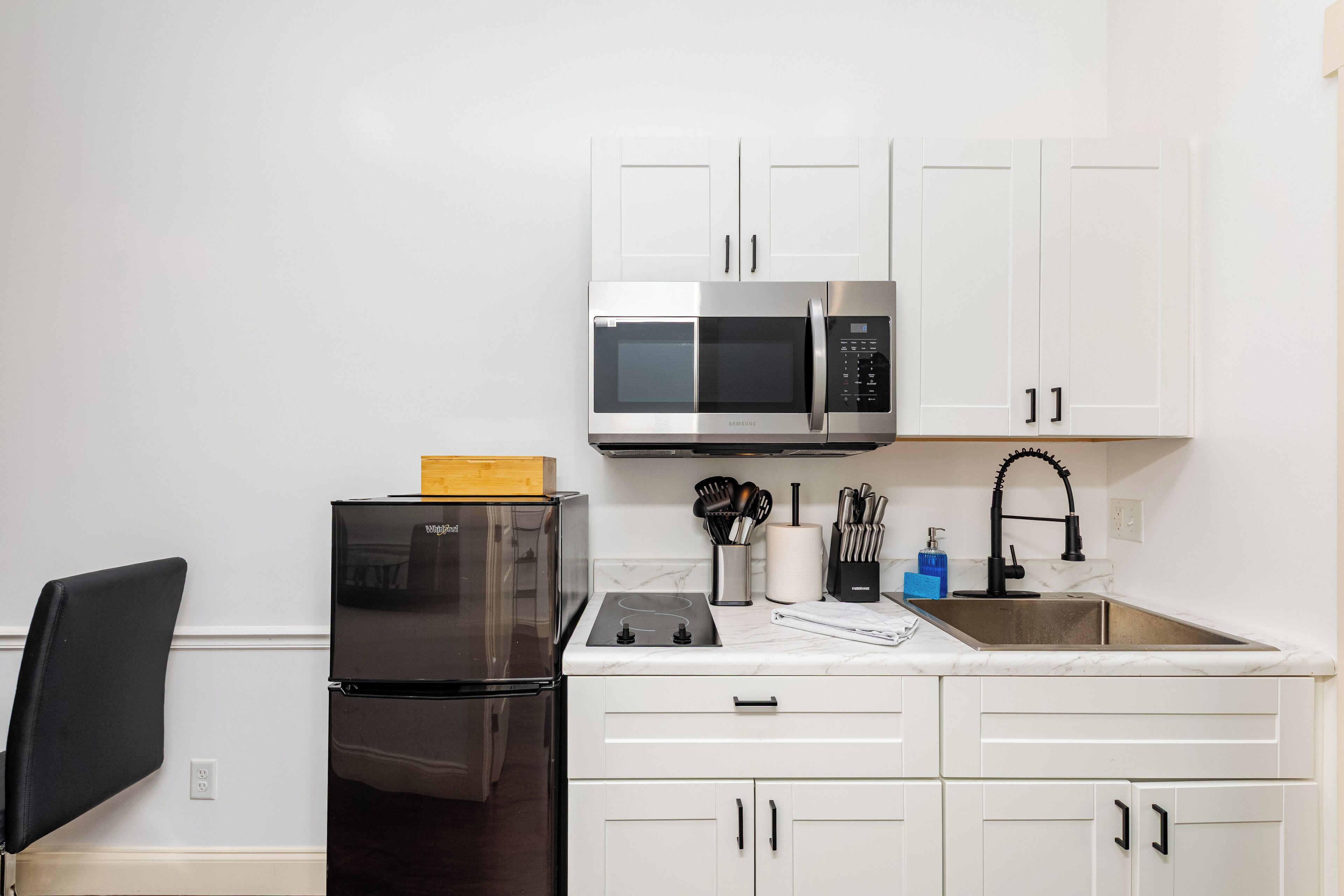 A modern kitchen with white cabinets, a stainless steel refrigerator, a microwave, and a sink.