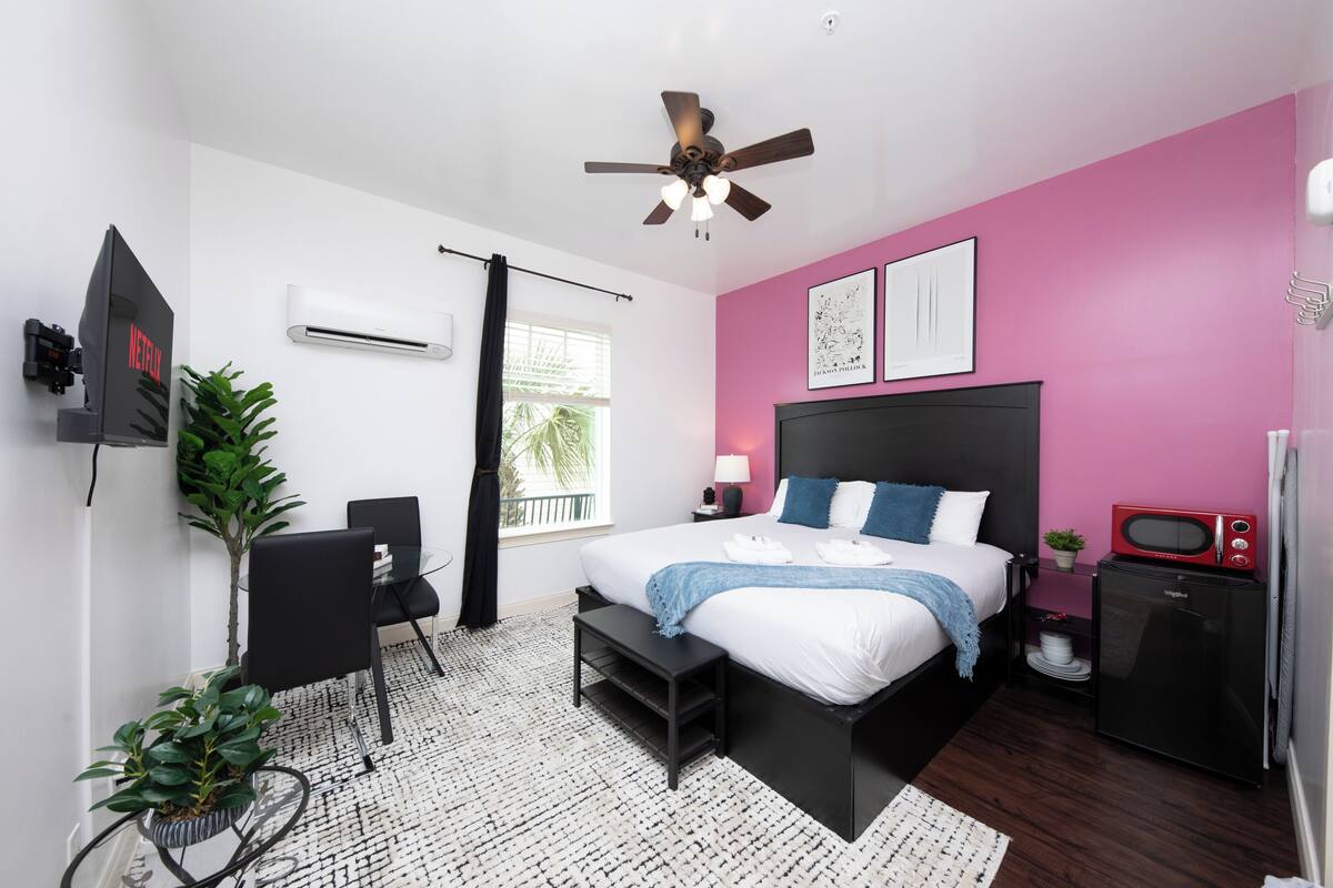 A modern bedroom with a bed, a ceiling fan, a TV, a microwave, and a small desk area.