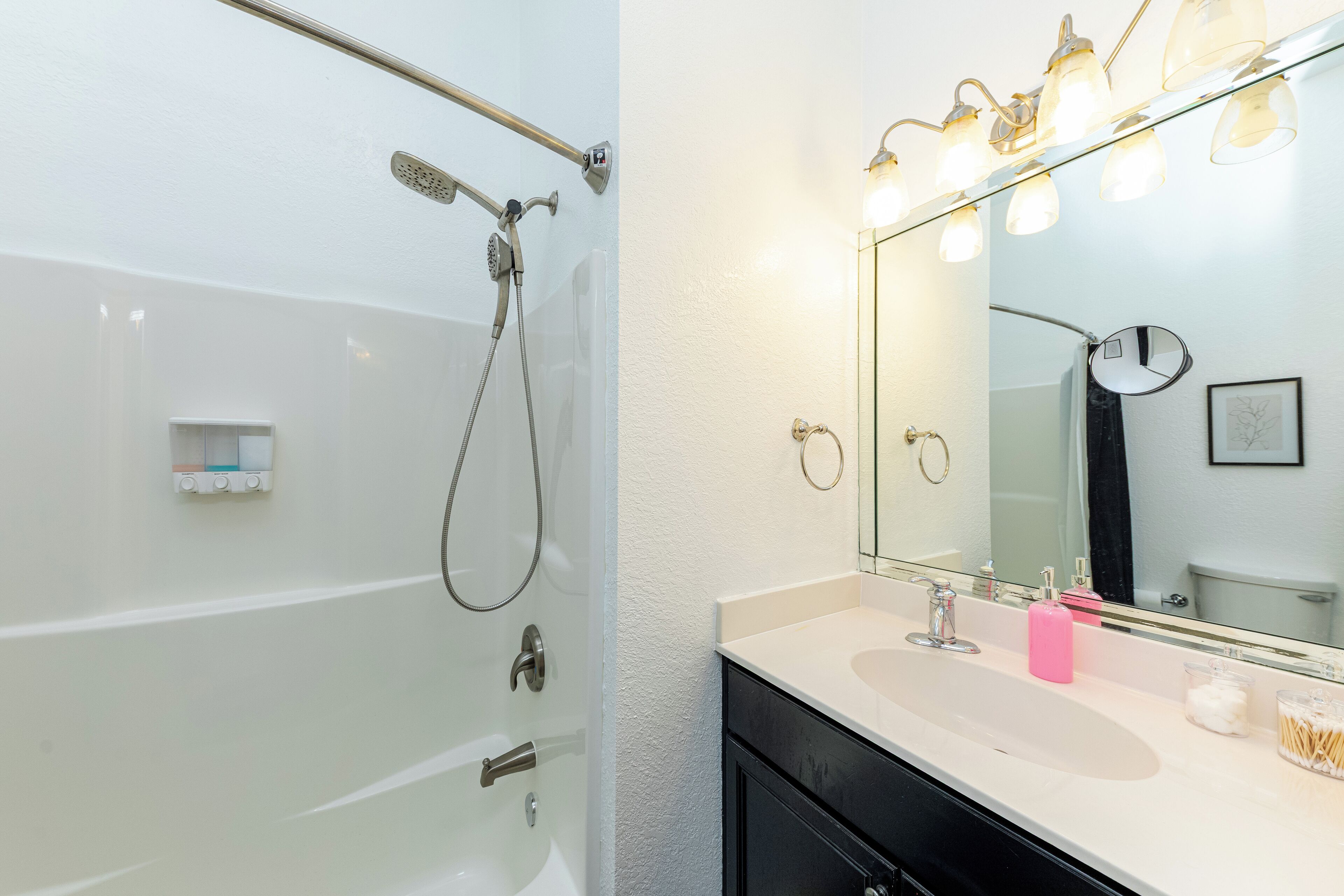 A bathroom with a bathtub, a sink with a mirror, and a shower with a handheld showerhead.