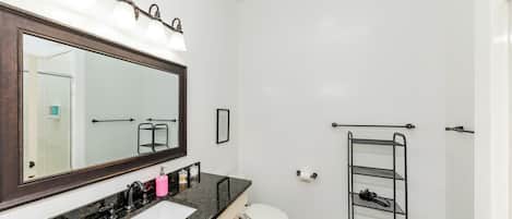 A bathroom with a large mirror, a sink, a toilet, and a metal shelf.