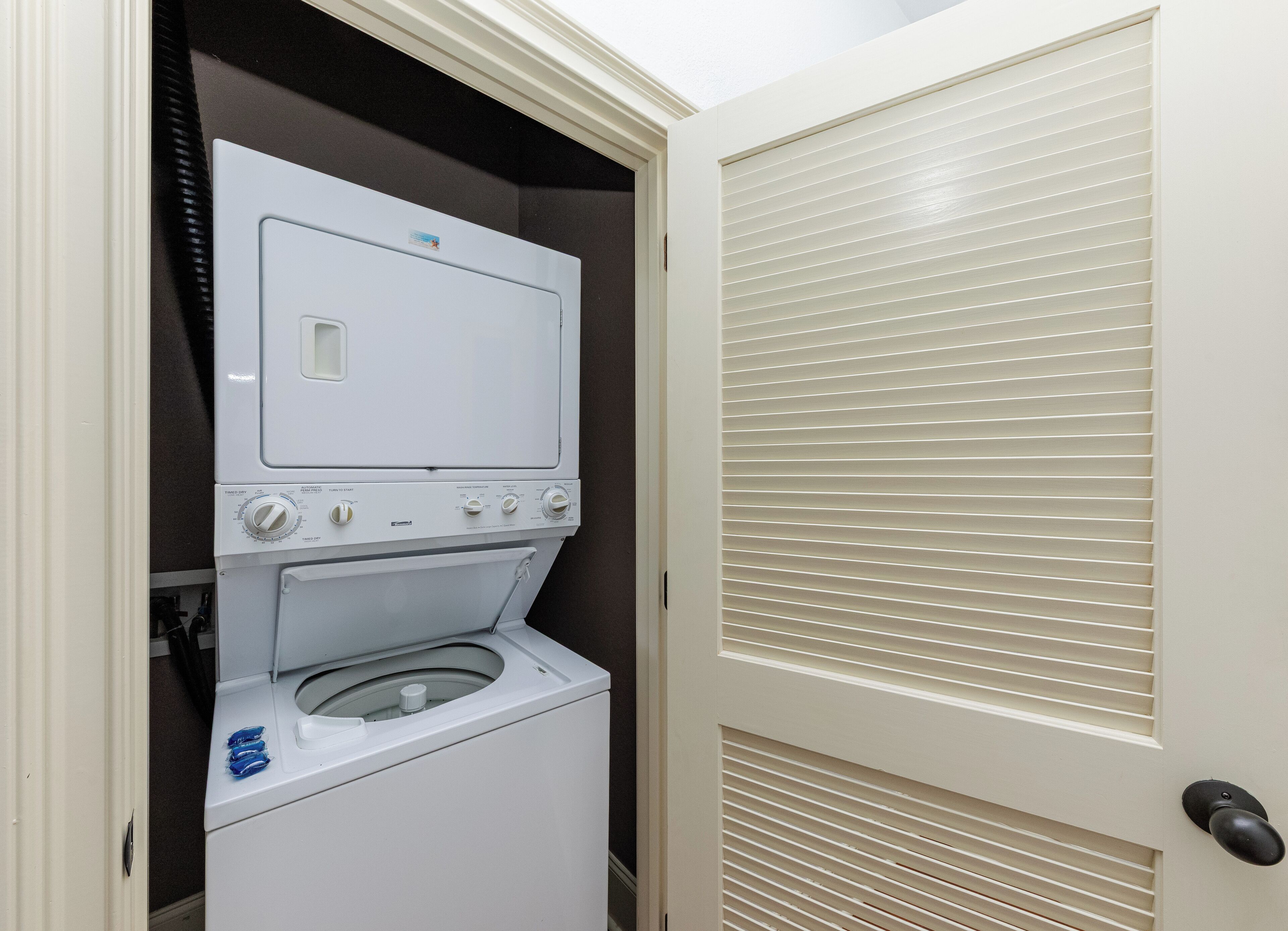 Uma lavanderia compacta com máquina de lavar e secadora de carregamento frontal, uma porta com janela e uma porta com ventilação.