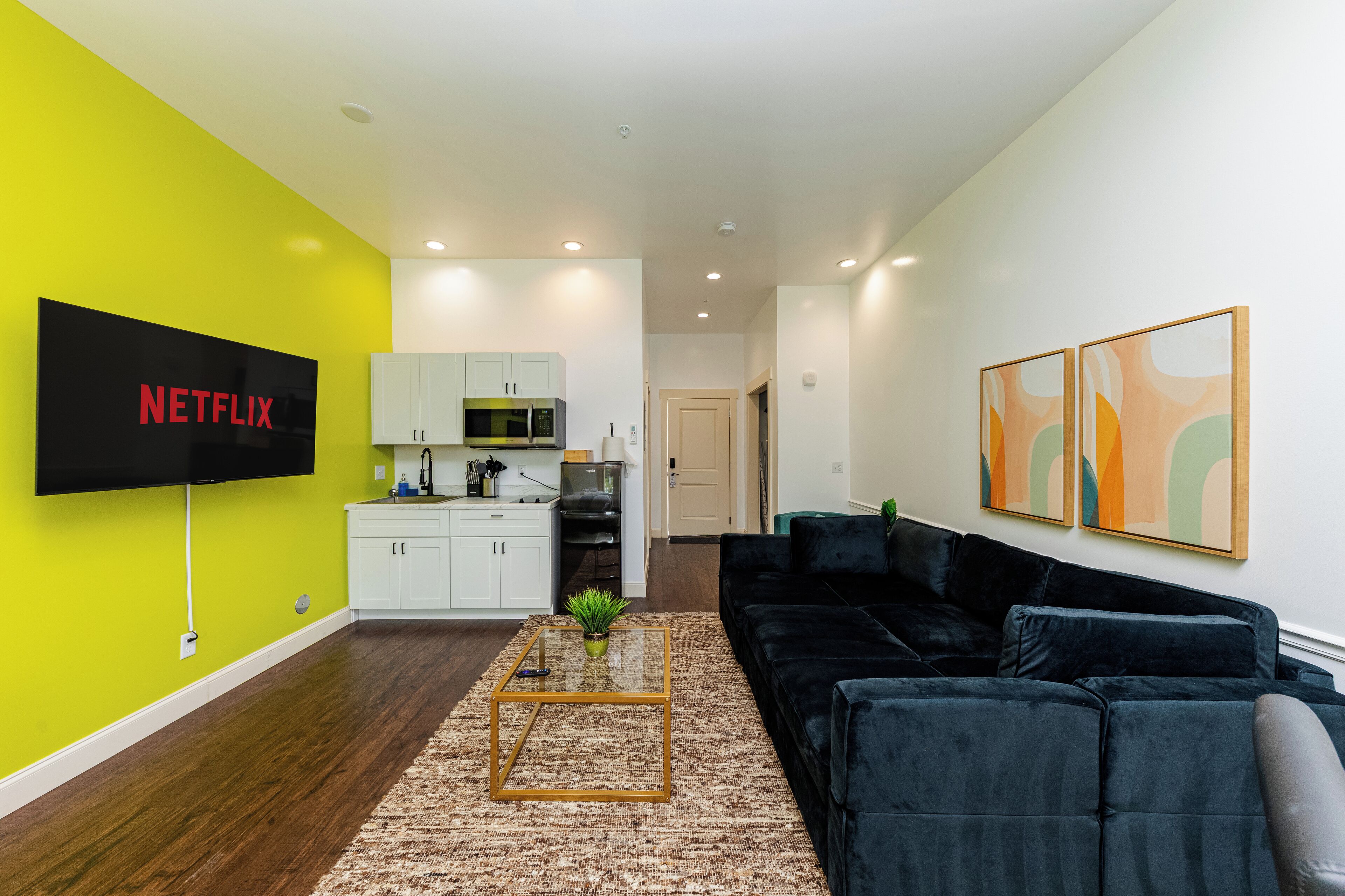 Una sala de estar moderna con un televisor de pantalla plana, un sofá negro, una mesa de centro y obras de arte en la pared.