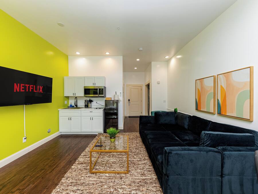 Ein modernes Wohnzimmer mit Flachbildfernseher, schwarzem Sofa, Couchtisch und Bildern an der Wand.