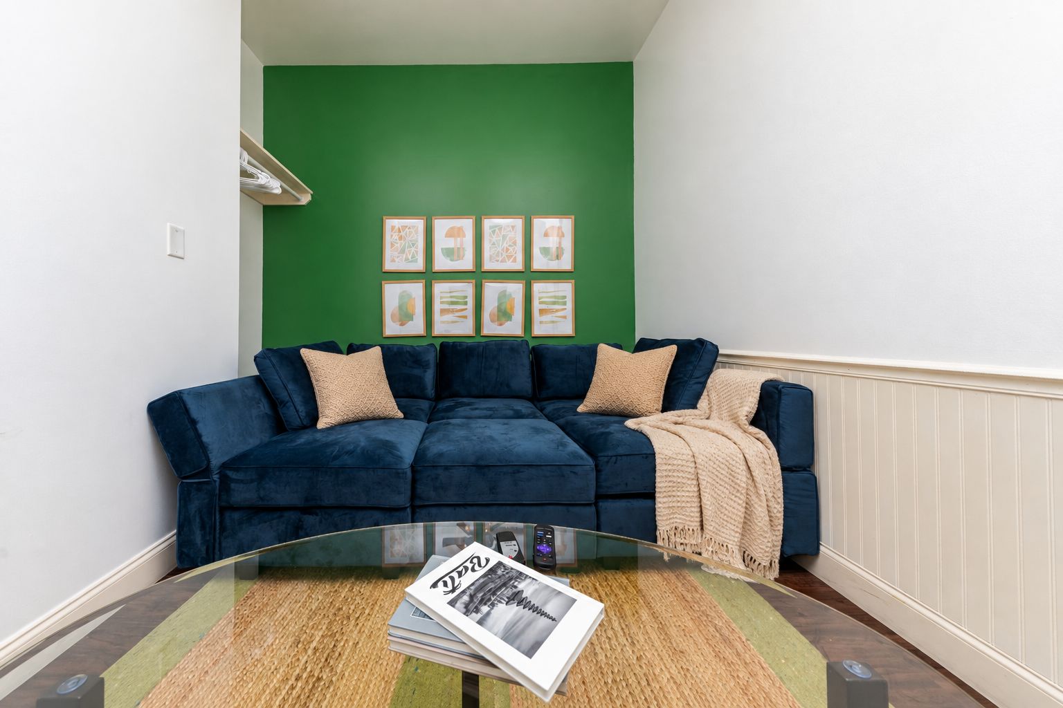 Una sala de estar con un sofá azul oscuro, una mesa de centro de vidrio y una pared de acento verde.