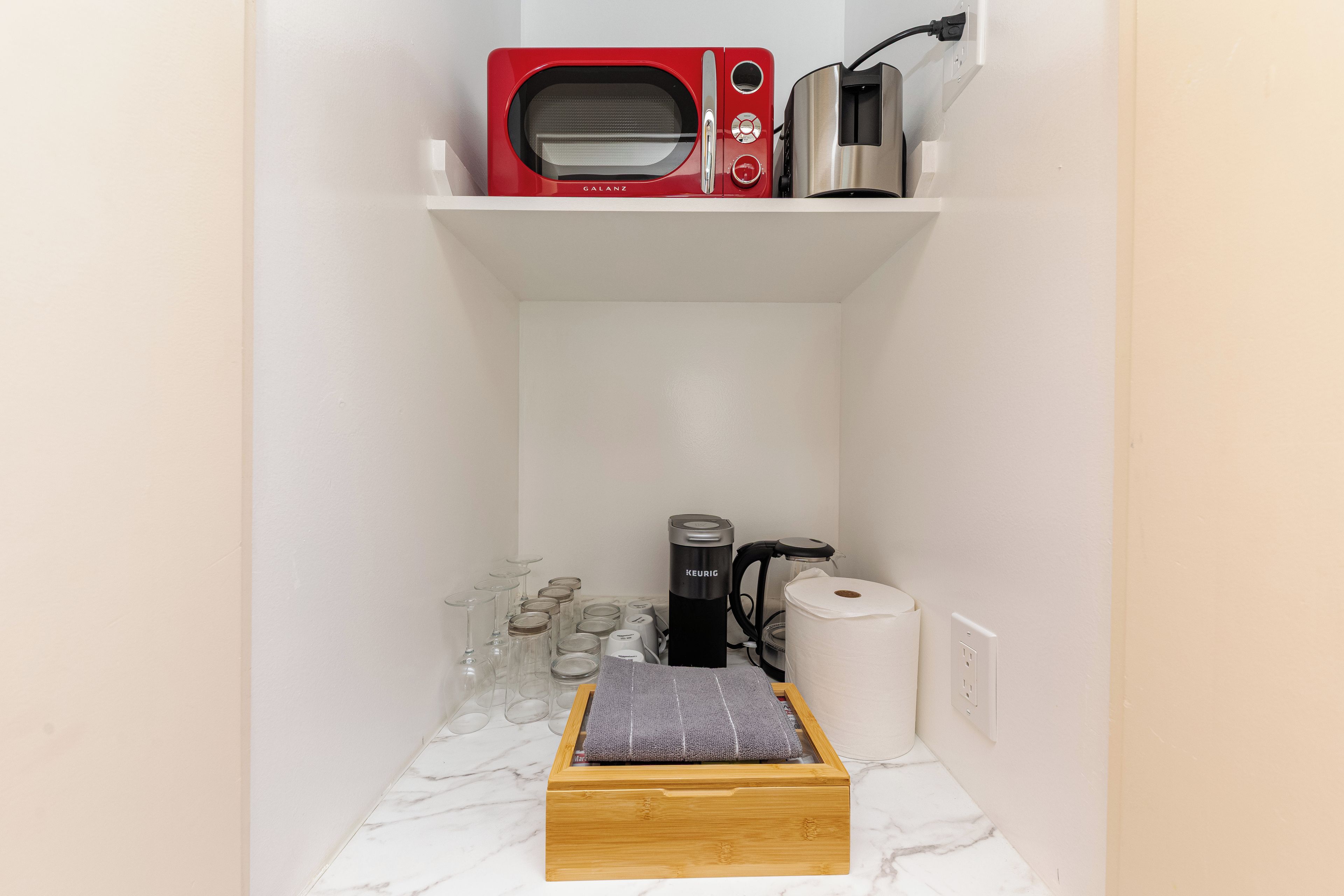 A compact kitchen area with a microwave, toaster, coffee maker, and a small wooden box on a marble countertop.