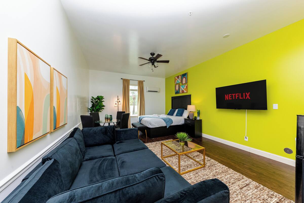 A modern living room with a black sofa, a coffee table, and a bed with a green wall and a Netflix sign.