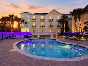 A hotel with a swimming pool, outdoor seating, and a sunset view.