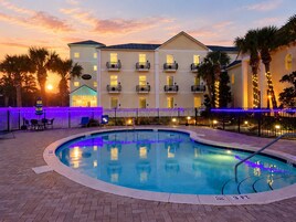 A hotel with a swimming pool, outdoor seating, and a sunset view.