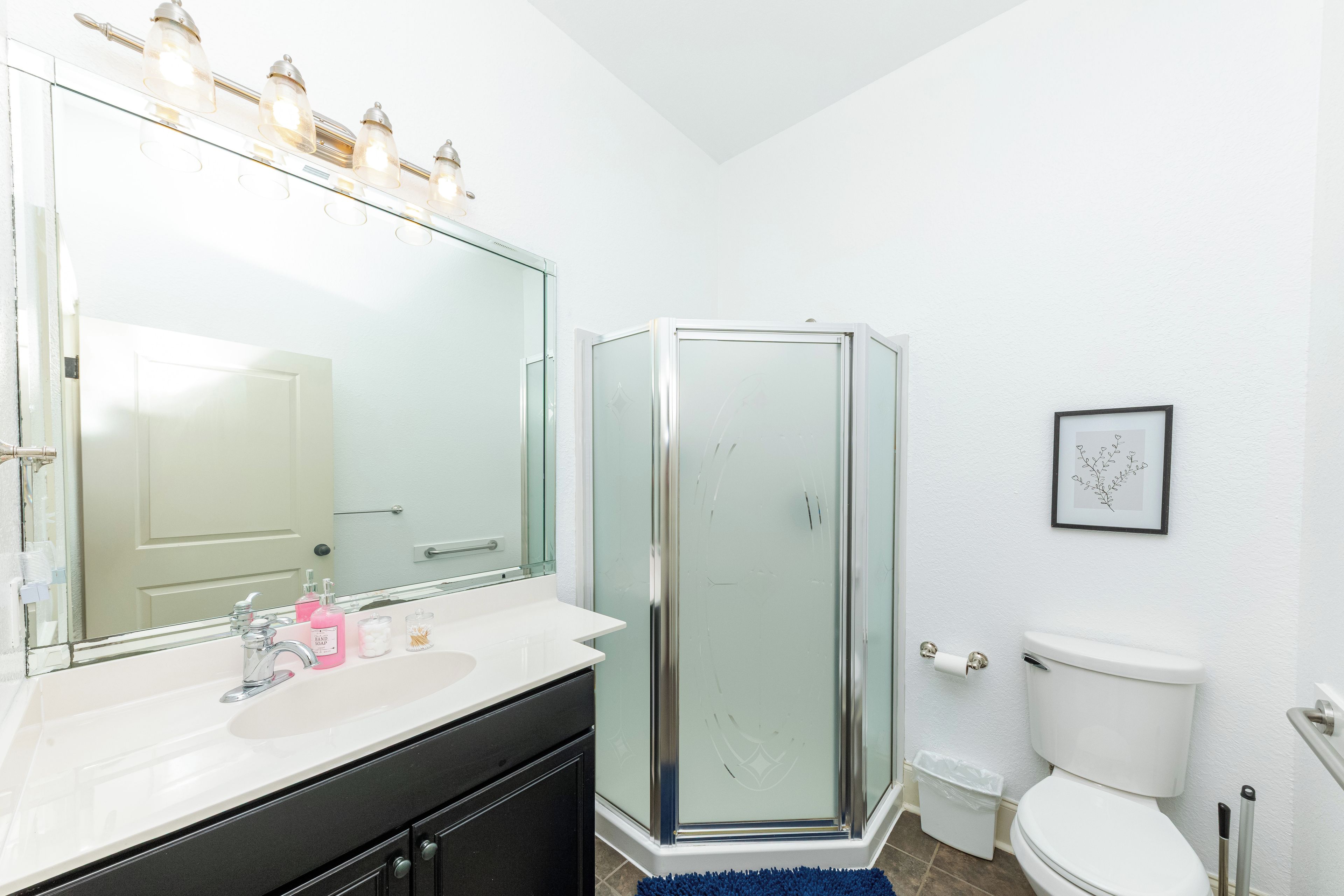 A bathroom with a glass-enclosed shower, a large mirror, a white sink, and a toilet.