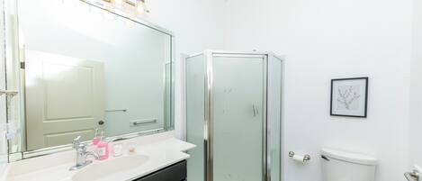 Un baño con ducha acristalada, un espejo grande, un lavabo blanco y un inodoro.