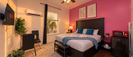 A modern bedroom with a bed, bedside table, air conditioning unit, ceiling fan, and a television displaying the Netflix logo.
