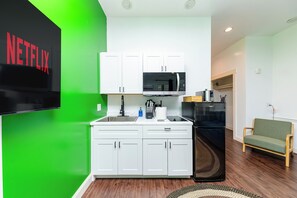 A modern kitchen with white cabinets, a black microwave, and a green accent wall. - 30A Inn & Suites (Santa Rosa Beach)