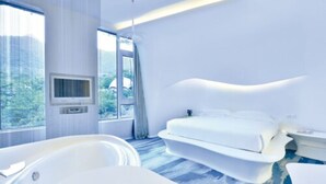 A modern hotel room with a large bed, a bathtub, and a television.