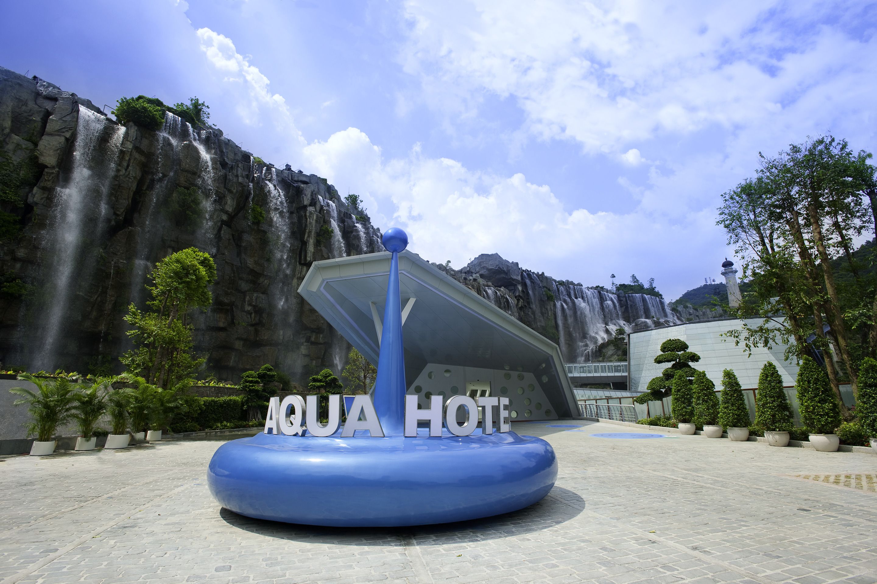A blue water feature with the text "AQUA HOTEL" in front of a waterfall and a modern building.