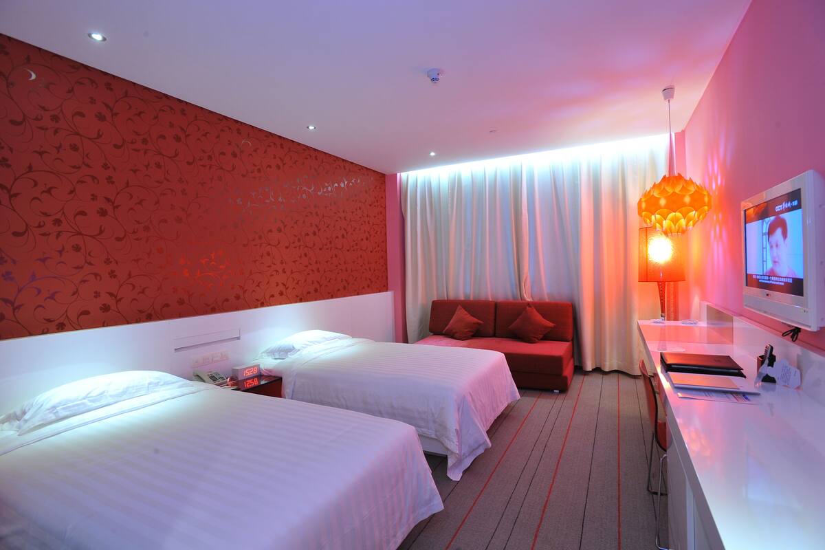 Habitación de hotel con dos camas, un sofá rojo, un escritorio con computadora y un televisor.