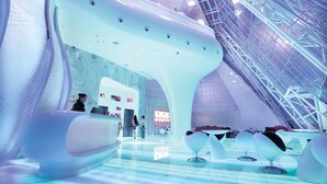 A futuristic interior with a large, white, organic-shaped reception area, a high ceiling with a glass structure, and modern seating arrangements.