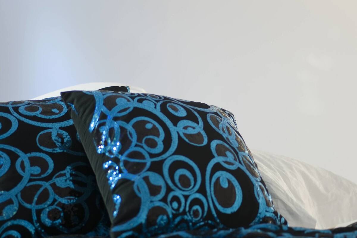 Una cama con almohadas estampadas y un cabecero blanco.