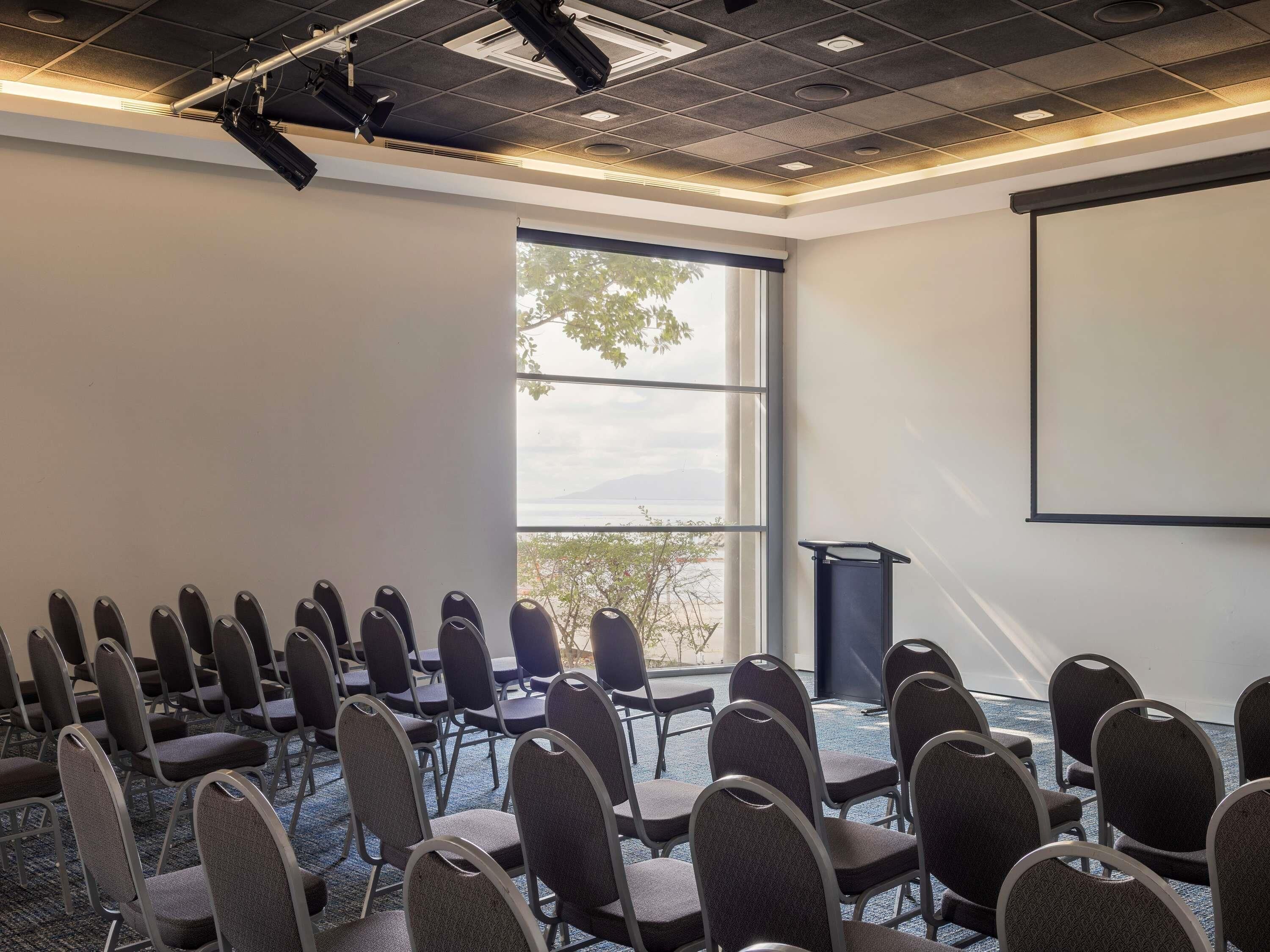 A conference room with rows of chairs, a projector screen, and a large window with a view of trees and mountains.