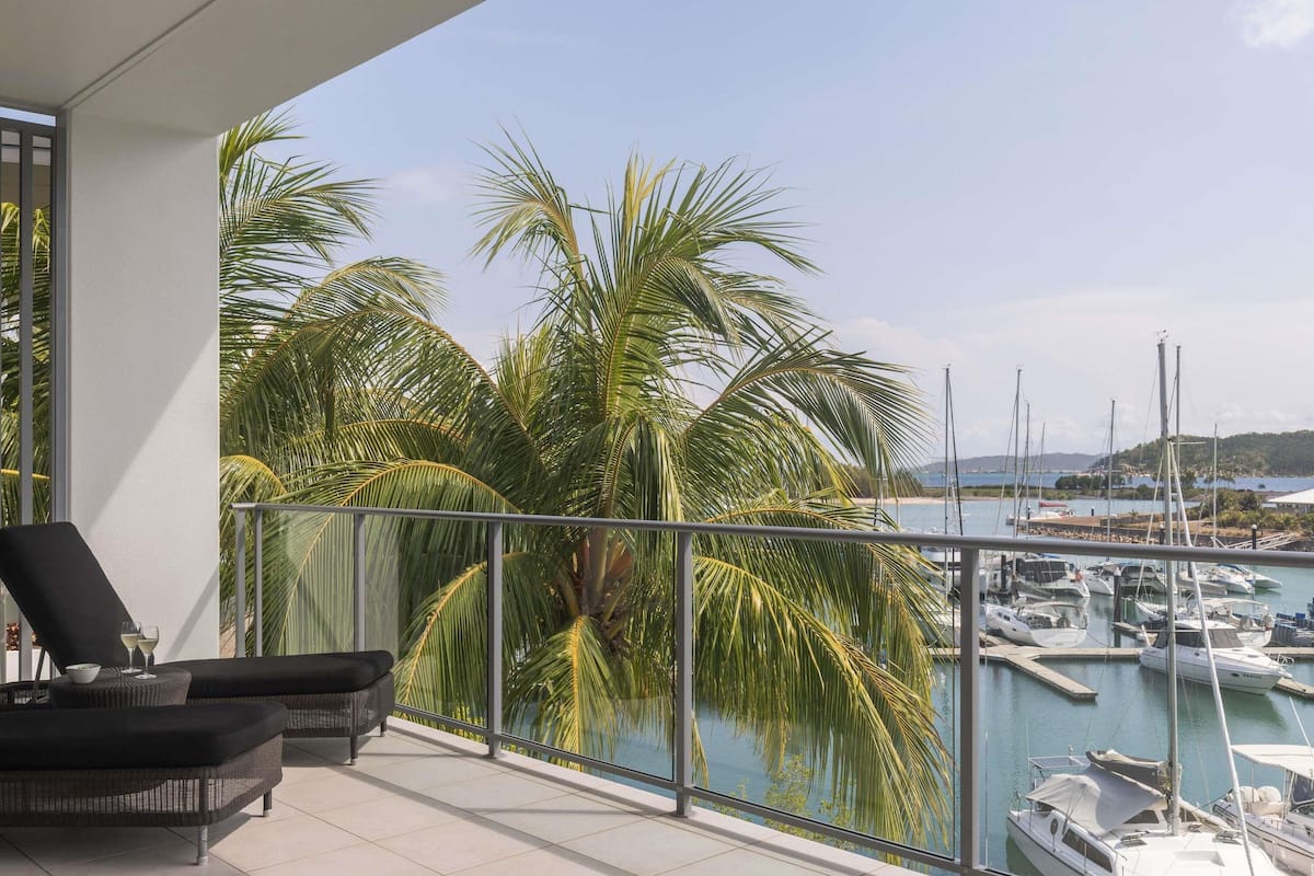 Un balcon offrant une vue sur un port de plaisance, des palmiers et un ciel dégagé.