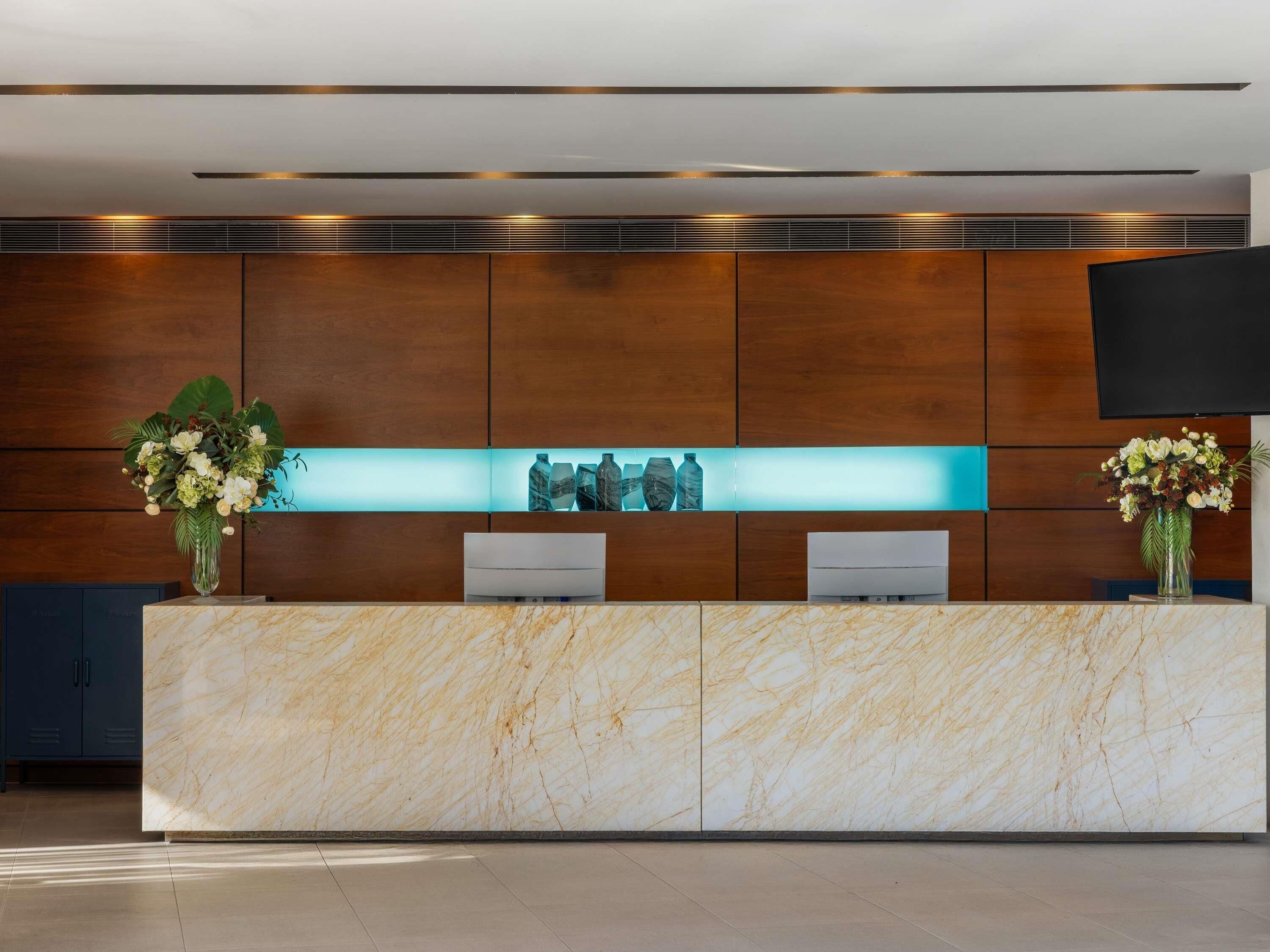 A reception desk with marble top, wooden panel walls, a flat-screen TV, and two flower arrangements.