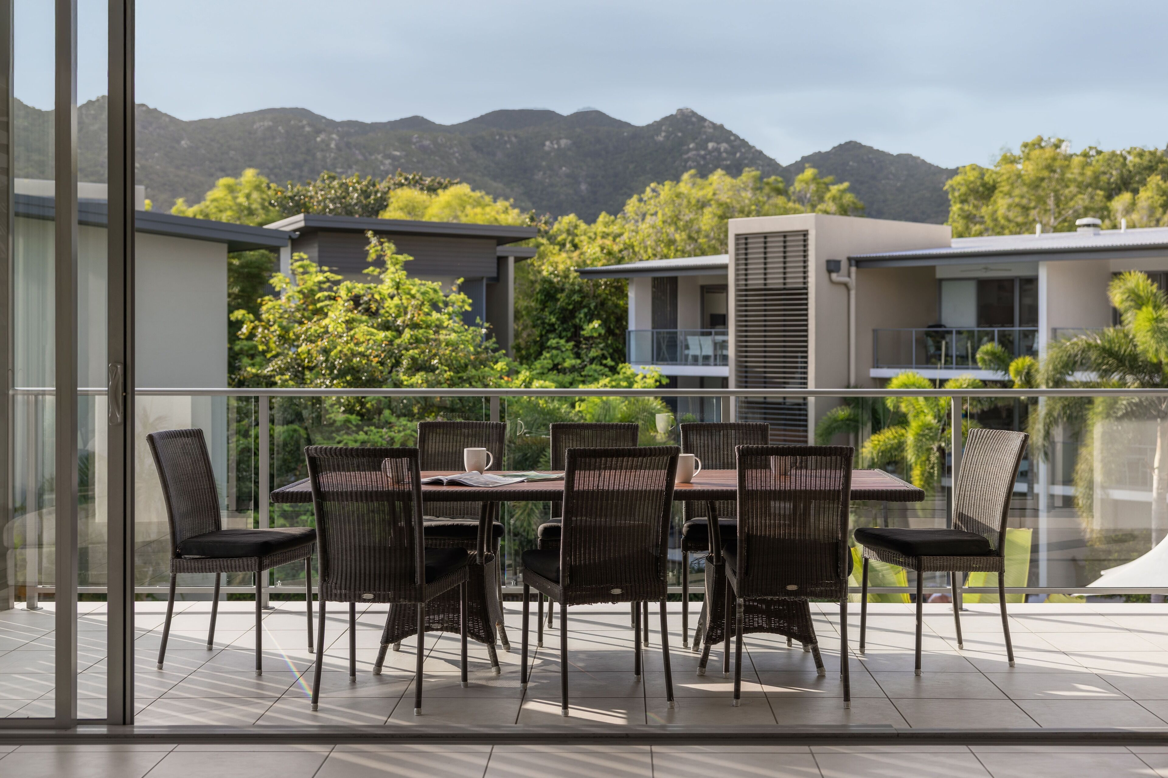 A modern outdoor dining area with a glass balustrade, wicker chairs, and a table set for six.