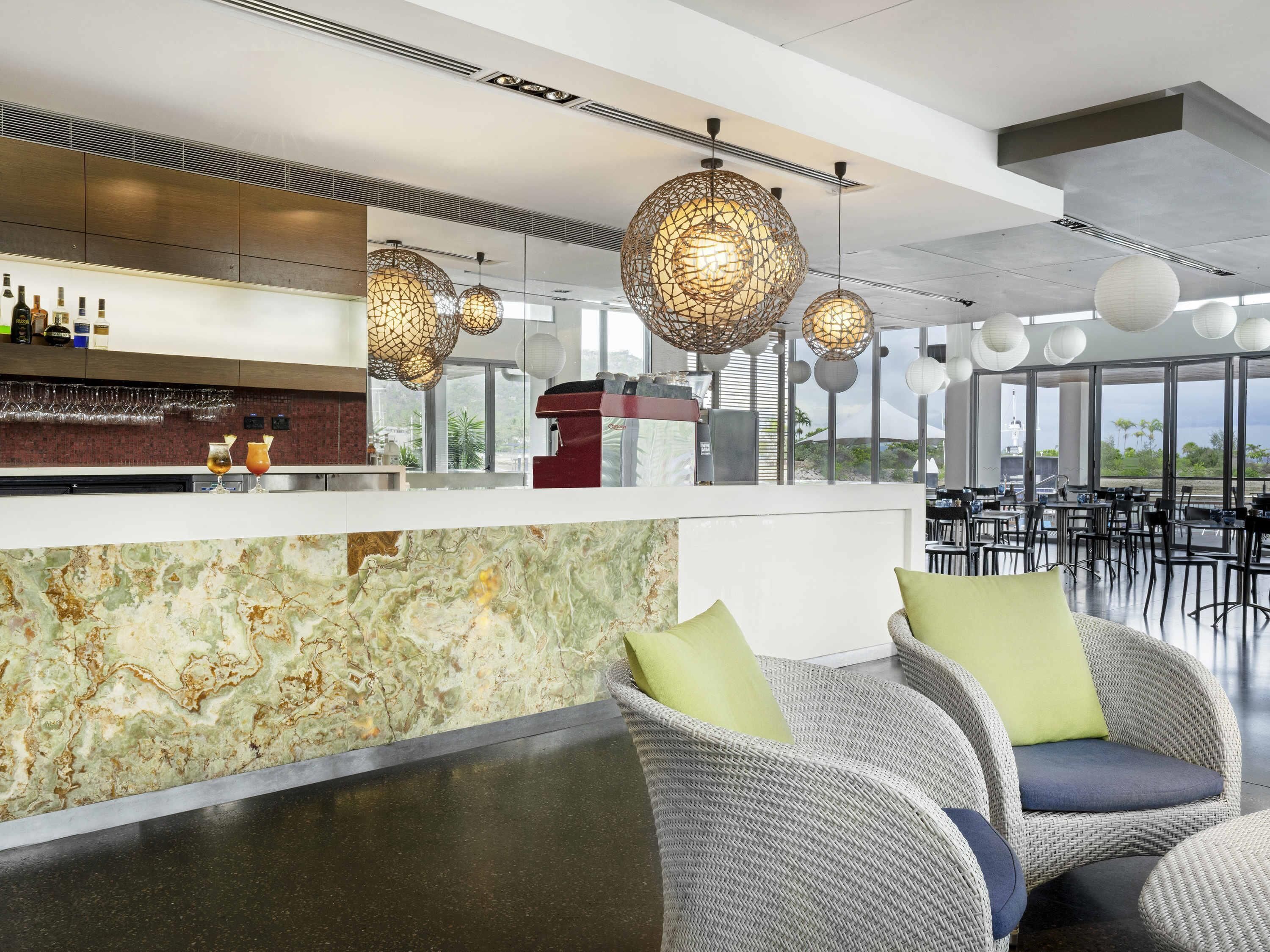 A modern bar area with a marble countertop, wicker chairs with cushions, and pendant lighting.