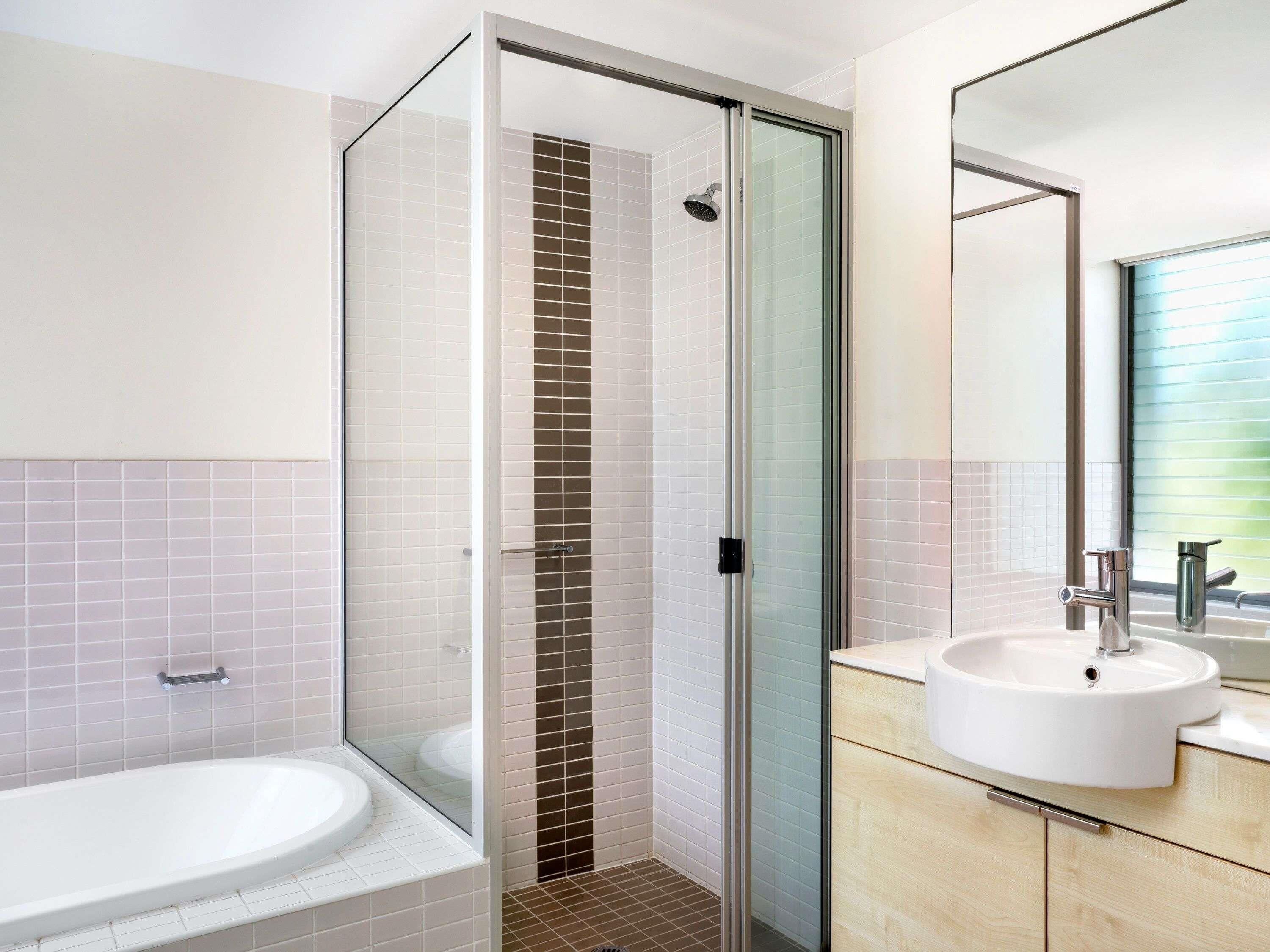 Un baño moderno con ducha envuelta en vidrio, una bañera blanca y un lavamanos con espejo.