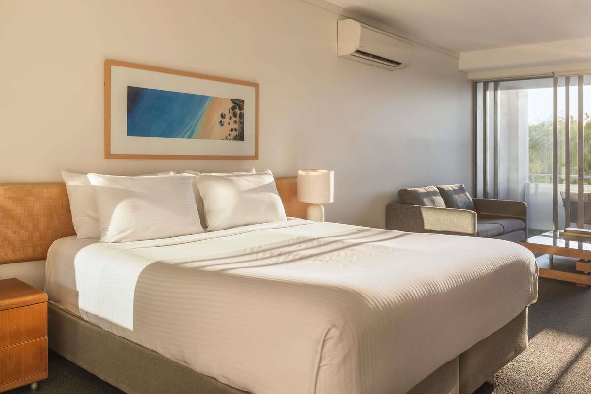 Une chambre d’hôtel avec un lit, une chaise, une table de chevet, une lampe et un tableau au mur.