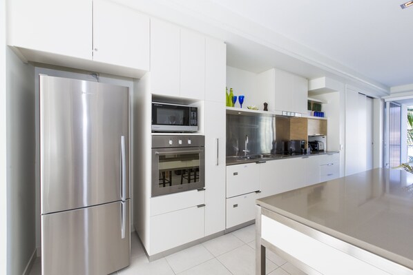 A modern kitchen with stainless steel appliances, white cabinetry, and a large countertop. - Peppers Blue on Blue (Nelly Bay)