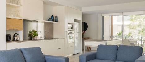 A modern living room with a sofa, a coffee table with magazines, and a kitchen area with cabinets and appliances.