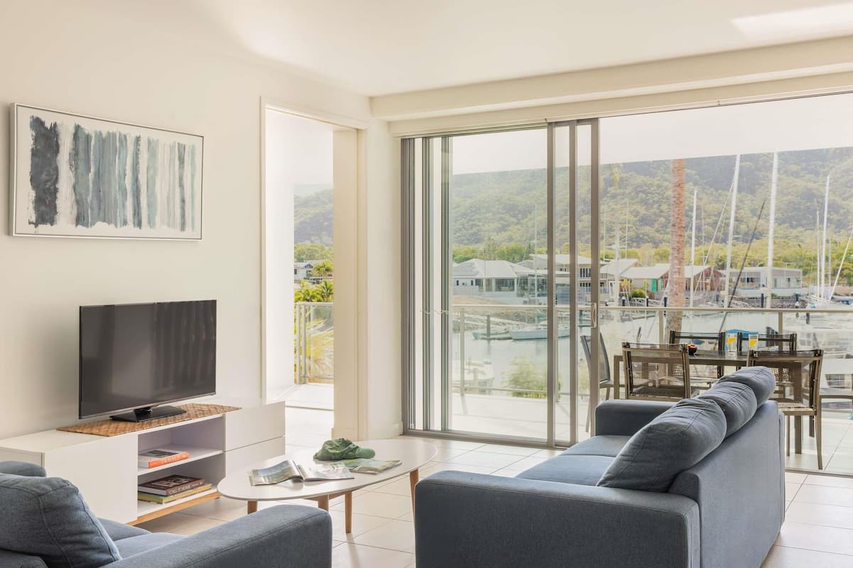 Un salon moderne avec un téléviseur, un canapé et une vue sur un port de plaisance.