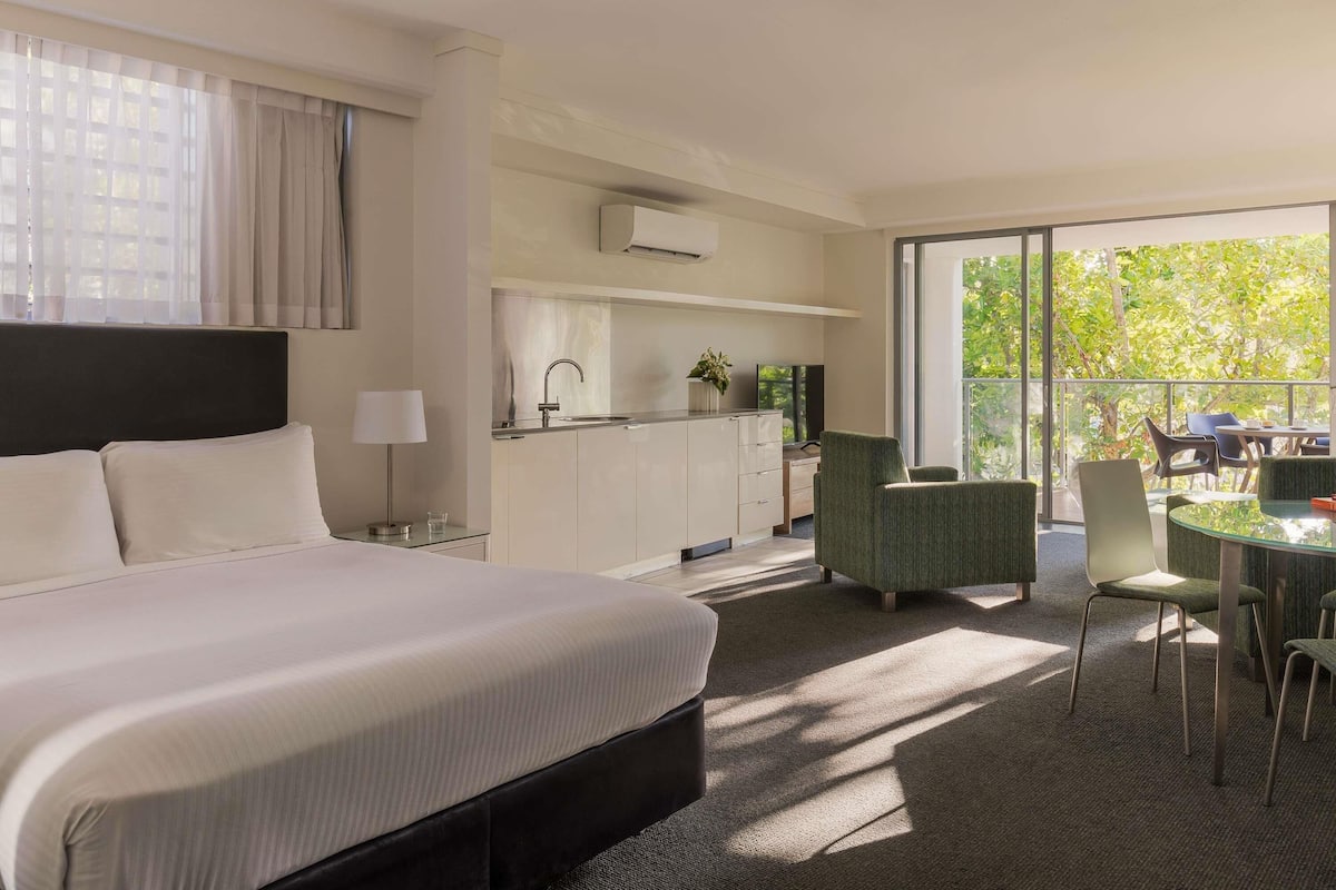 Une chambre d’hôtel comprenant un lit, un bureau, une chaise, une petite table et un balcon avec vue sur les arbres.