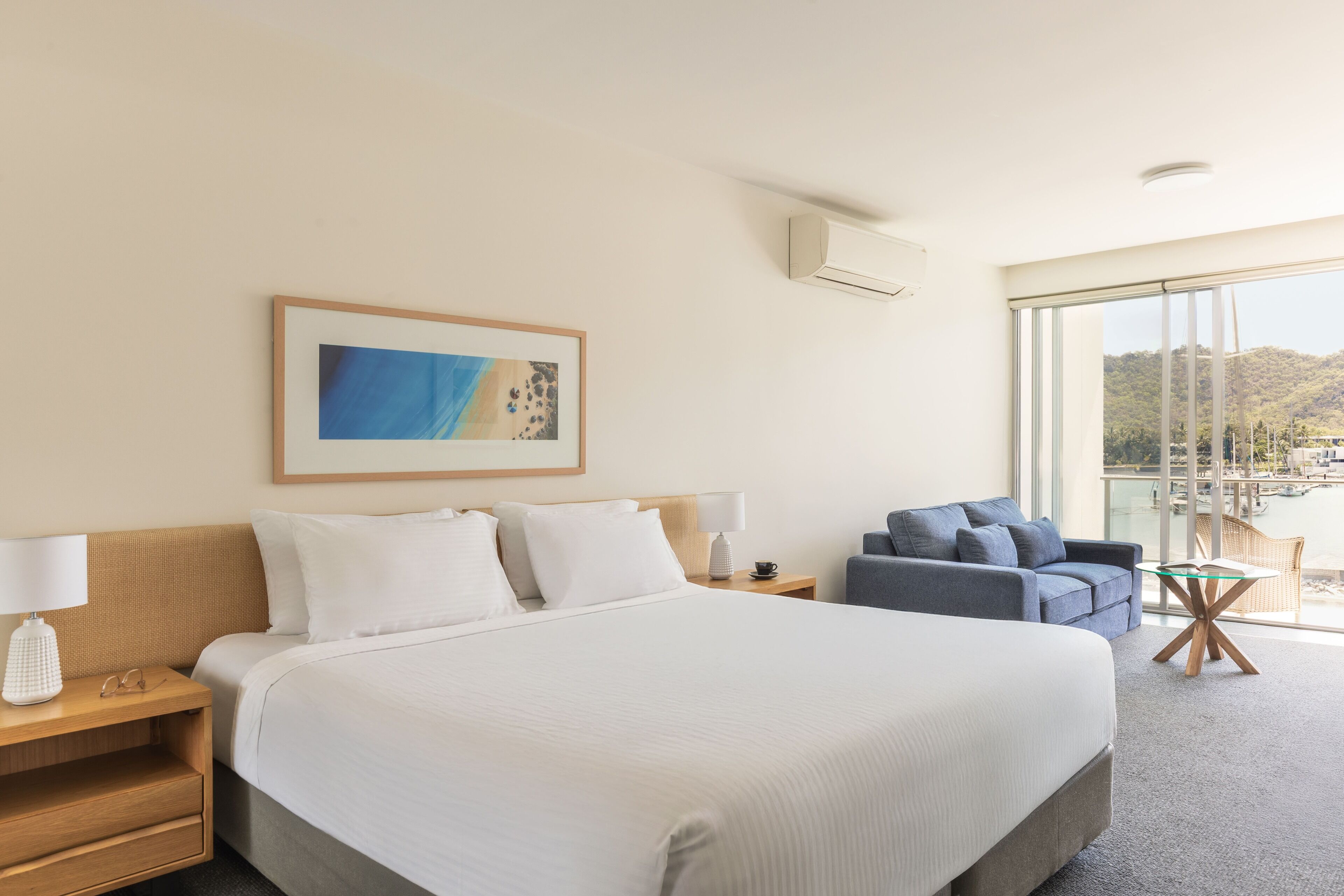 Habitación de hotel con una cama grande, un sofá, una mesita y una ventana con vistas a las montañas.