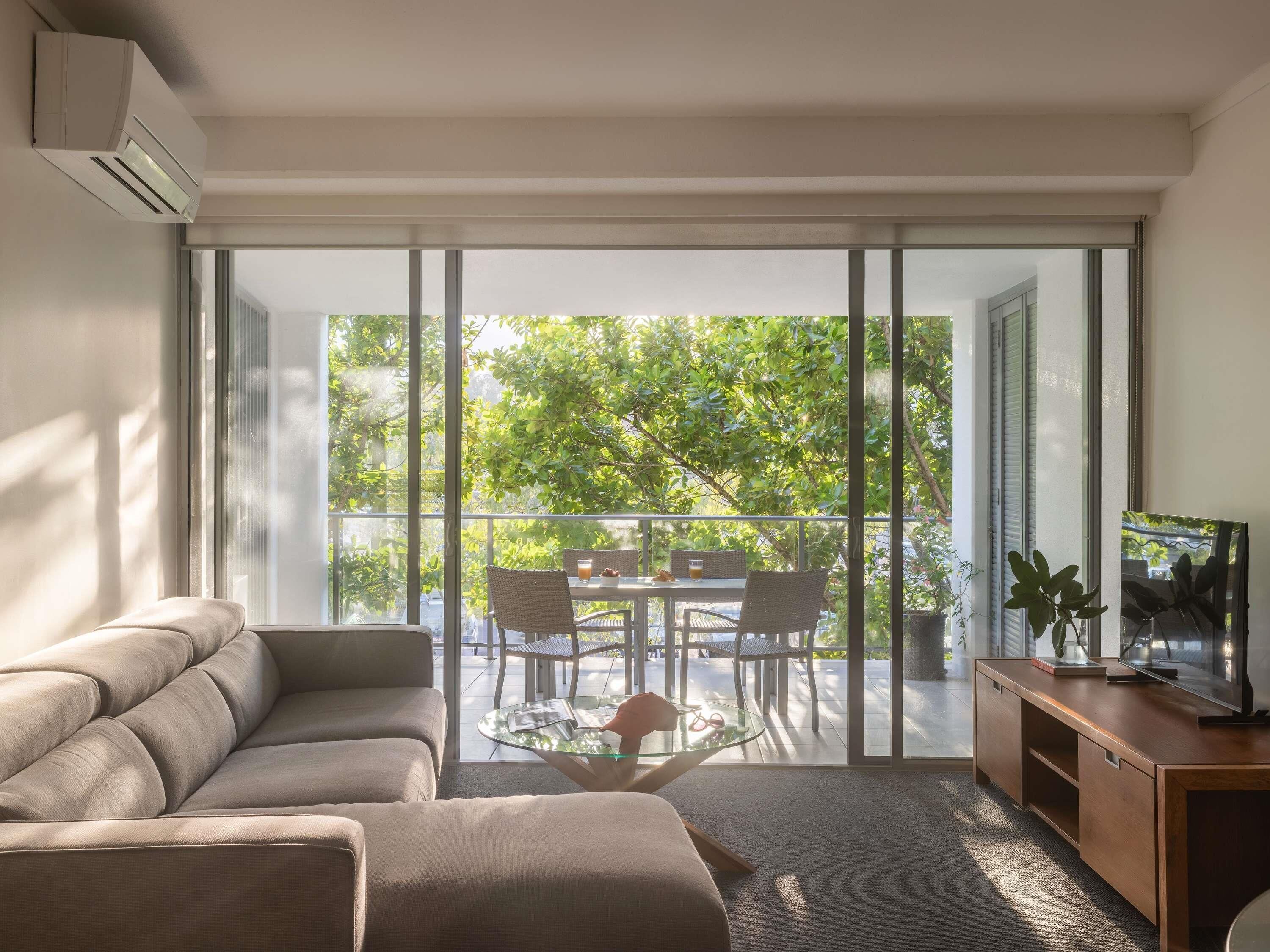 Una sala moderna con un sofá, una mesa de centro de vidrio y un mueble bajo para la televisión de madera.