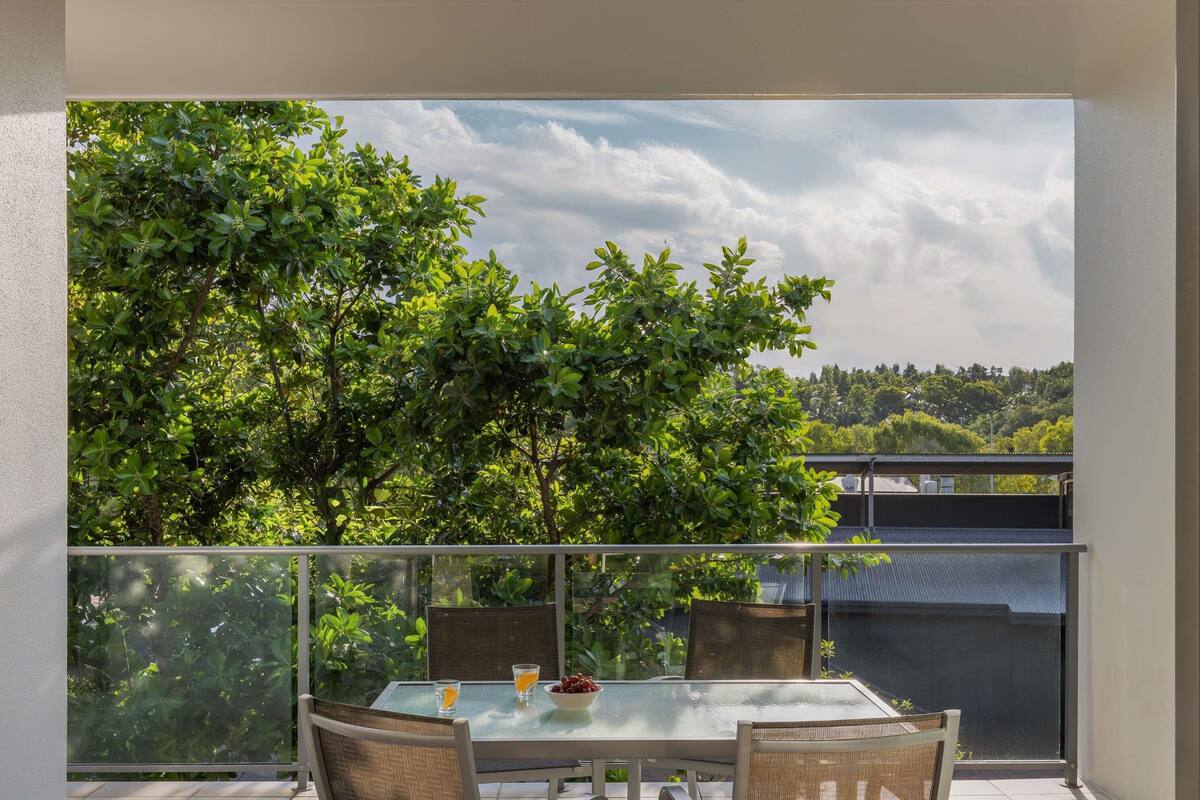 Un balcon doté d’une table et de chaises en verre, offrant une vue sur un paysage verdoyant et luxuriant.