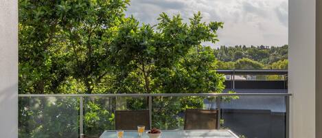 A balcony with a glass table and chairs, overlooking a lush green landscape.