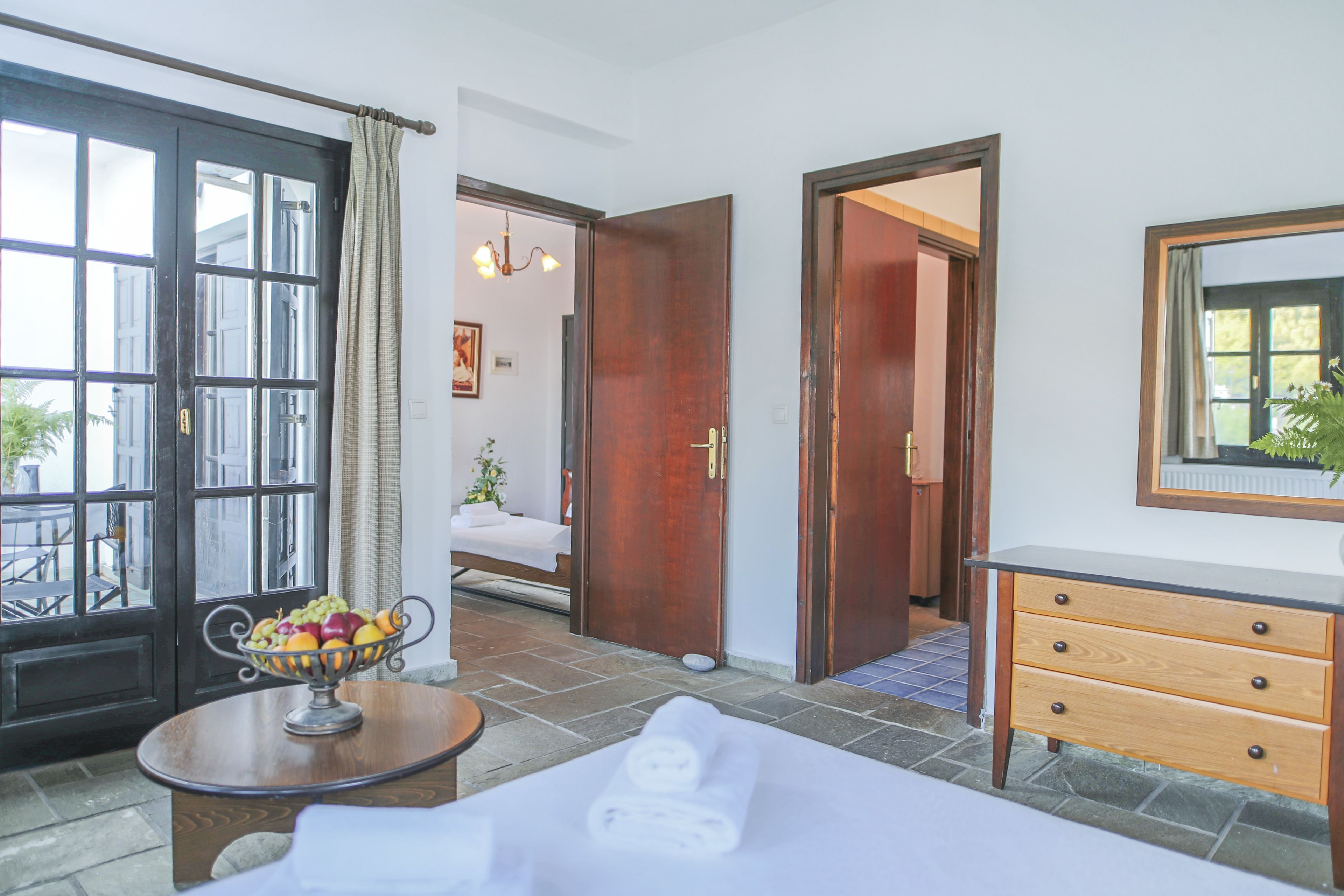A hotel room with a bed, a bedside table with a fruit bowl, a wooden dresser, and a large mirror.