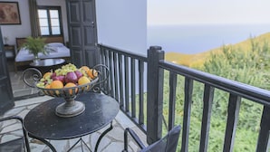 Un balcón con una mesa que sostiene un frutero, vista al mar, y una habitación con una cama y una planta.